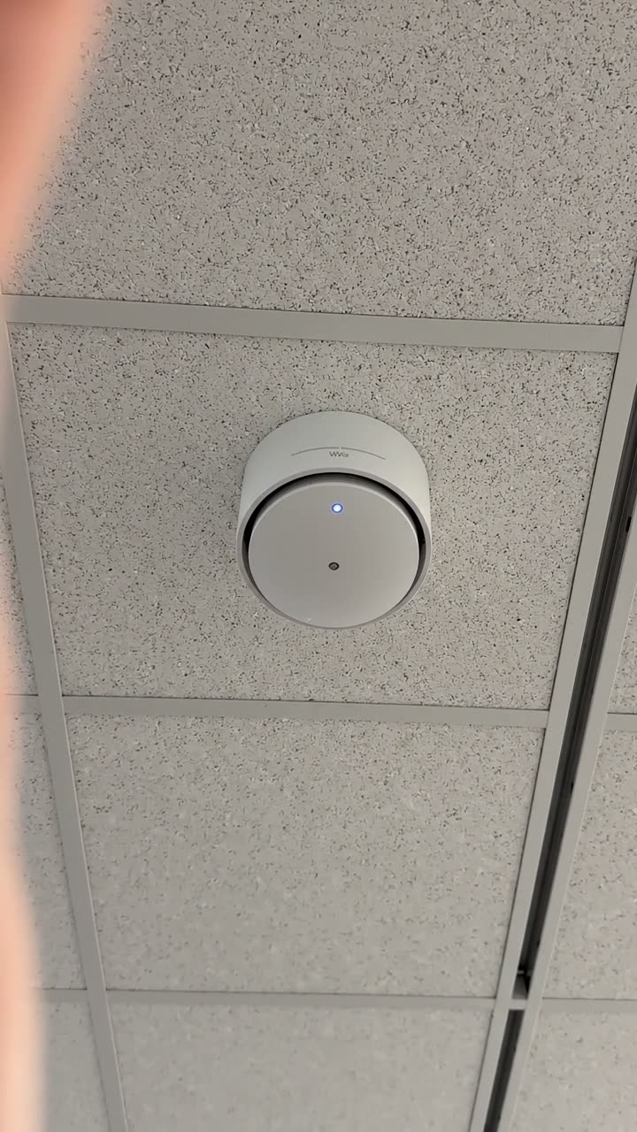 A wireless access point on a ceiling grid with its status light on