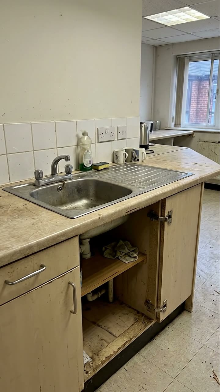 An office kitchenette with a worn worktop and missing cupboard doors