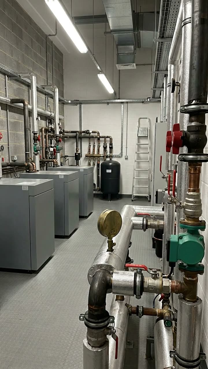 A row of boilers in a plant room with labelled valves and pipework