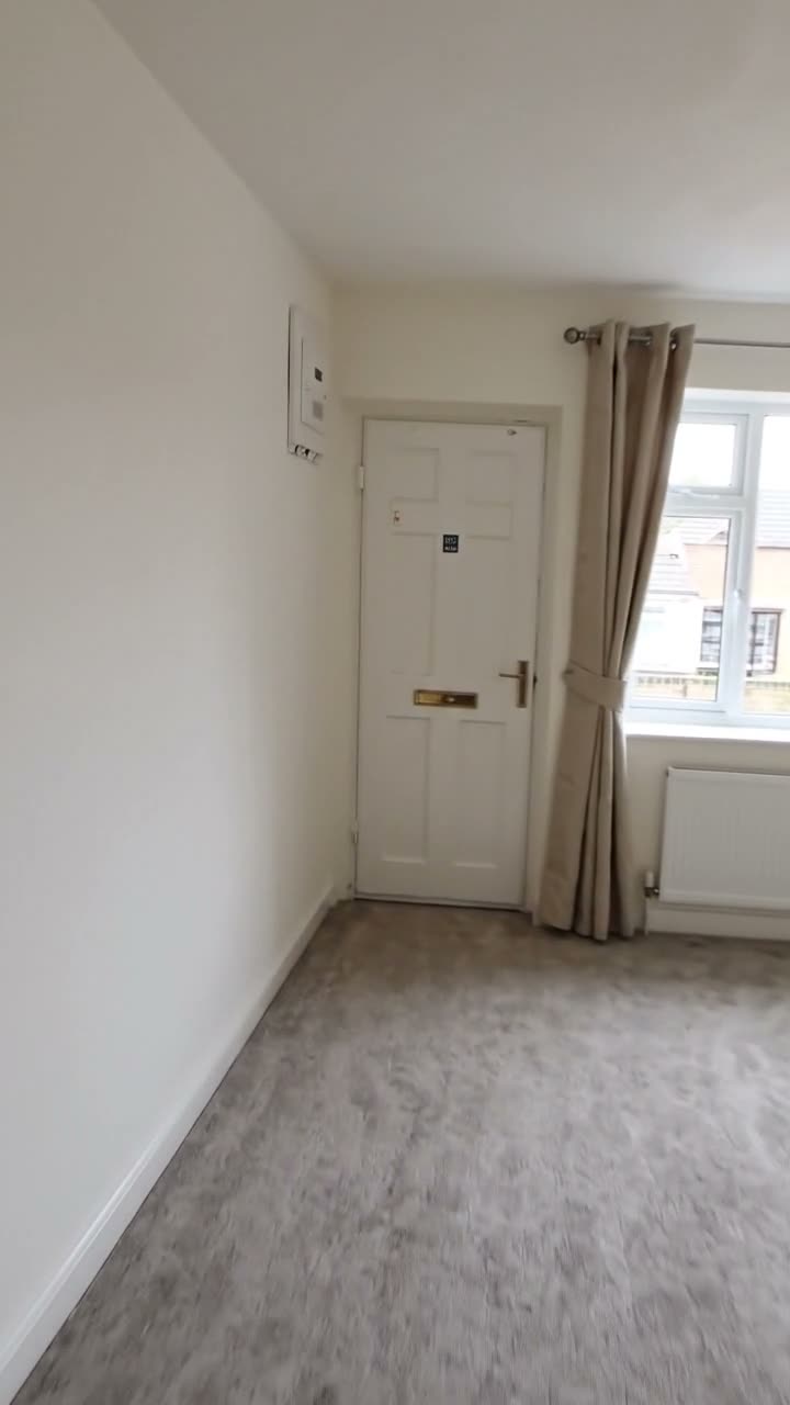 An empty living room showing the carpet, walls, door, curtains and window